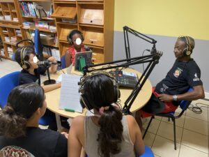 Gramoun Sello, au studio radio, devant son micro est interviewé par 4 élèves.