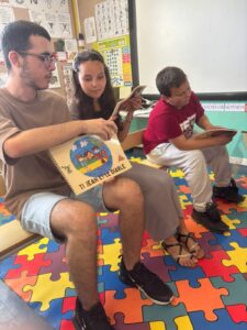 3 collégiens (2 garçons et une fille) sont assis sur de petites chaises et montrent un livre. 